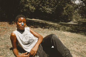 African-American with Nöz applied to her nose laying on the grass in surrounded by thickly grown tree in an open field.